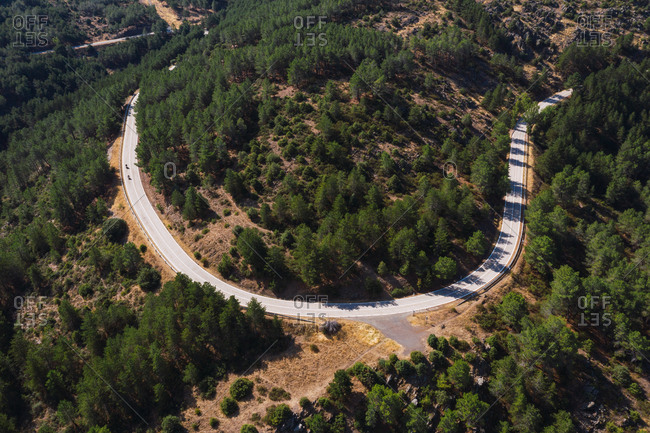 Drone view of bikers riding motorcycles along empty roadway in mountainous area on sunny day