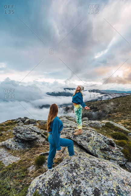 Side view of traveling female friends standing on rocks and enjoying freedom in highlands during vacation