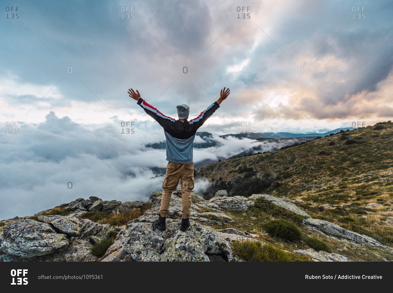 Back view of male hiker standing with outstretched arms on top of hill and enjoying freedom in highlands during adventure