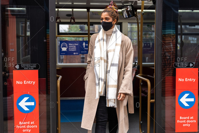 Concentrated young African American lady in stylish clothes and face mask commuting on public transport during coronavirus