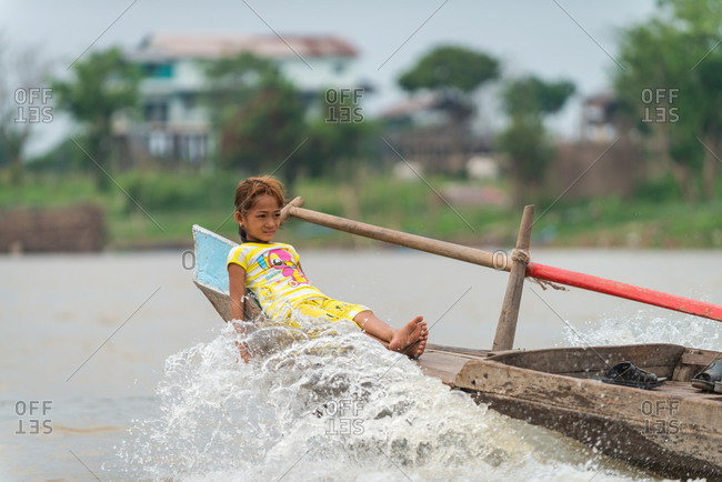 Floating Village, Kompong Chnang, Cambodia - 24 February 2013: Young Khmer Girl Relaxes On Bow Of Traditional Wooden Fishing Boat And Cools Her Hand In Wake Water.