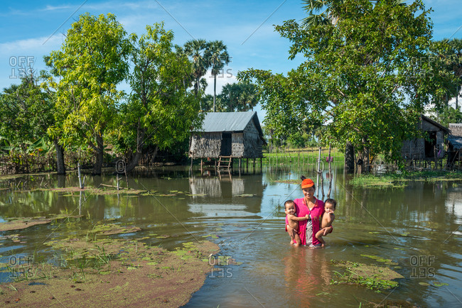 Flooded Houses, Kompong Thom, Cambodia - 17 October 2013: Mother Carries 2 Young Children From Her Flooded House In Rainy Season.