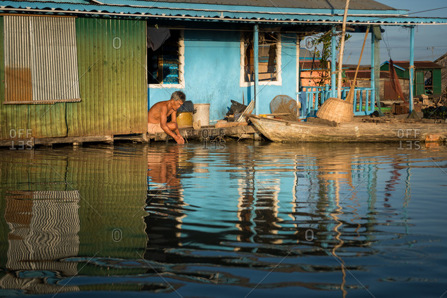 Floating Village, Kompong Chnang, Cambodia - 15 December 2014: Elder Khmer Washes On The Doorstep Of His Floating House In Warm Evening Light.