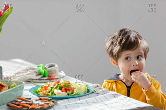 Little boy sitting at easter dinner table and eating a salad