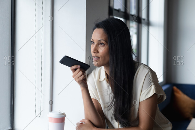 Mixed race businesswoman standing by window using smartphone in modern office. business modern office workplace technology.