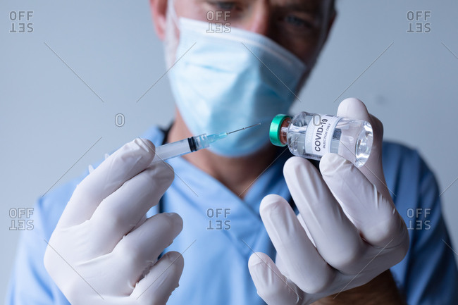 Caucasian male doctor wearing face mask standing and filling syringe. medical professional healthcare worker hygiene during coronavirus covid 19 pandemic.