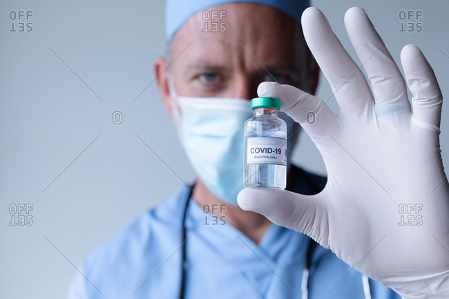 Caucasian male doctor wearing face mask standing and showing coronavirus vaccine. medical professional healthcare worker hygiene during coronavirus covid 19 pandemic.