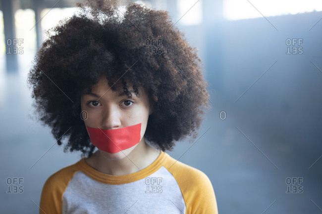Mixed race woman with tape on mouth looking at camera. gender fluid lgbt identity racial equality concept.