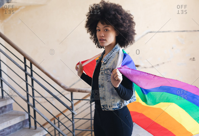 Mixed race woman holding a rainbow flag looking at camera. gender fluid lgbt identity racial equality concept.