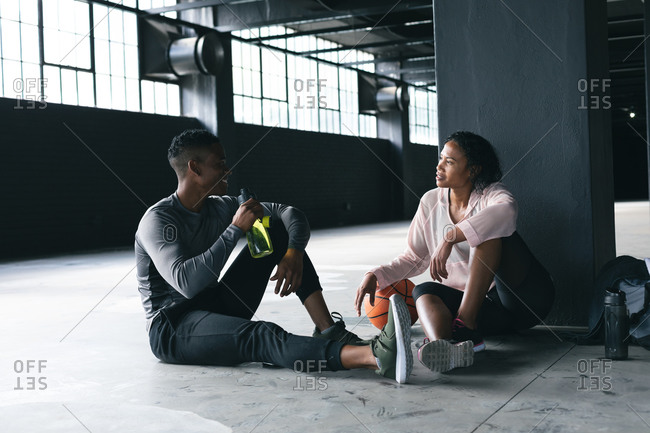African American man and woman sitting in empty urban building and resting after playing basketball. drinking water and talking. urban fitness healthy lifestyle.