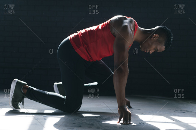 African American man wearing sports clothes kneeling starting to run in empty urban building. urban fitness healthy lifestyle.