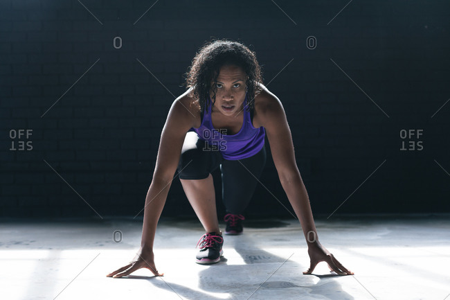 African American woman wearing sports clothes kneeling starting to run in empty urban building. urban fitness healthy lifestyle.