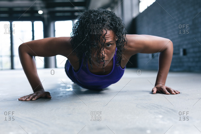 African American woman wearing sports clothes doing push ups in empty urban building. urban fitness healthy lifestyle.