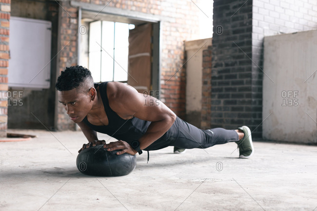 African American man exercising doing push ups on a medicine ball in empty urban building. urban fitness healthy lifestyle