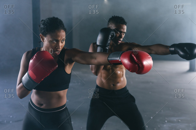 African American man and woman wearing boxing gloves throwing punches in air in empty building. urban fitness healthy lifestyle.