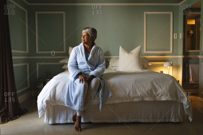 Senior African American woman sitting on a bed in a sleeping room. retirement lifestyle in self isolation during coronavirus covid 19 pandemic.