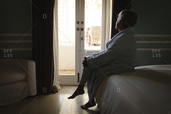 Senior African American woman sitting on a bed looking through window in a sleeping room. retirement lifestyle in self isolation during coronavirus covid 19 pandemic.