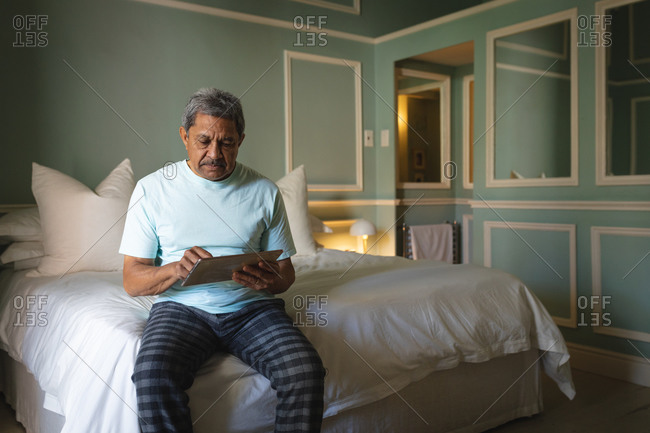 Senior African American man sitting on a bed using digital tablet in a sleeping room. retirement lifestyle in self isolation during coronavirus covid 19 pandemic.