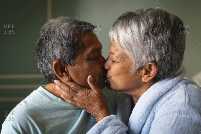 Senior African American man sitting on a bed kissing in a sleeping room. retirement lifestyle in self isolation during coronavirus covid 19 pandemic.