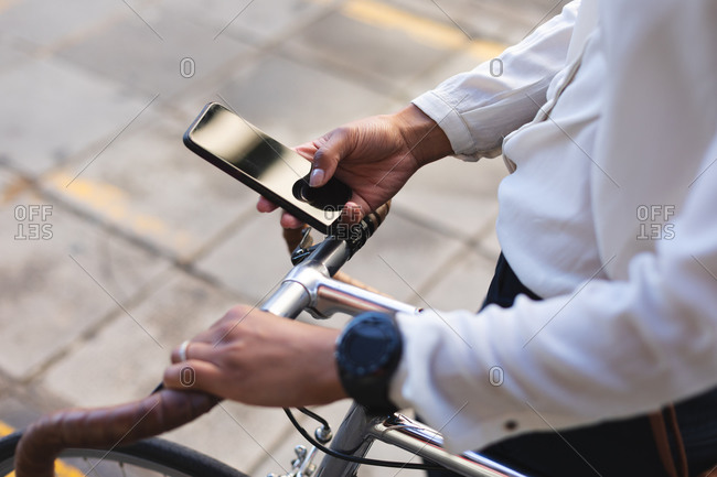 Mid section of African American woman with bicycle using smartphone on the street. lifestyle living concept during coronavirus covid 19 pandemic.