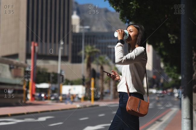 African American woman with smartphone drinking coffee on the street. lifestyle living concept during coronavirus covid 19 pandemic.