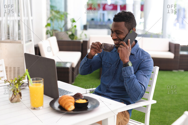African American man sitting in a cafe talking using smartphone and drinking coffee. businessman on the go out in the city.