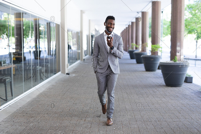 African American male businessman walking wearing face mask talking on smartphone. businessman on the go out in the city.