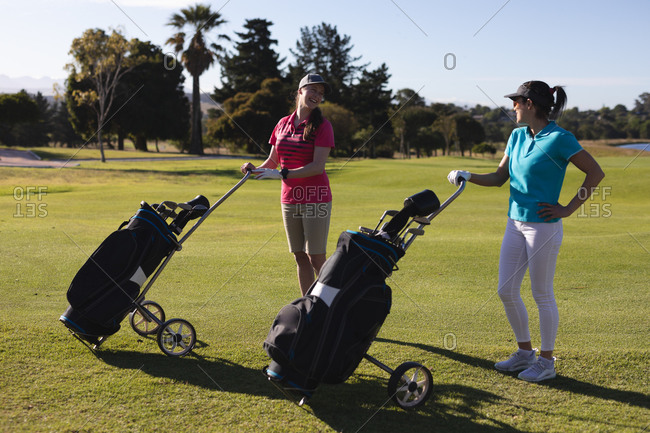 Two caucasian women on golf course holding golf bags and talking. sport leisure hobbies golf healthy outdoor lifestyle.