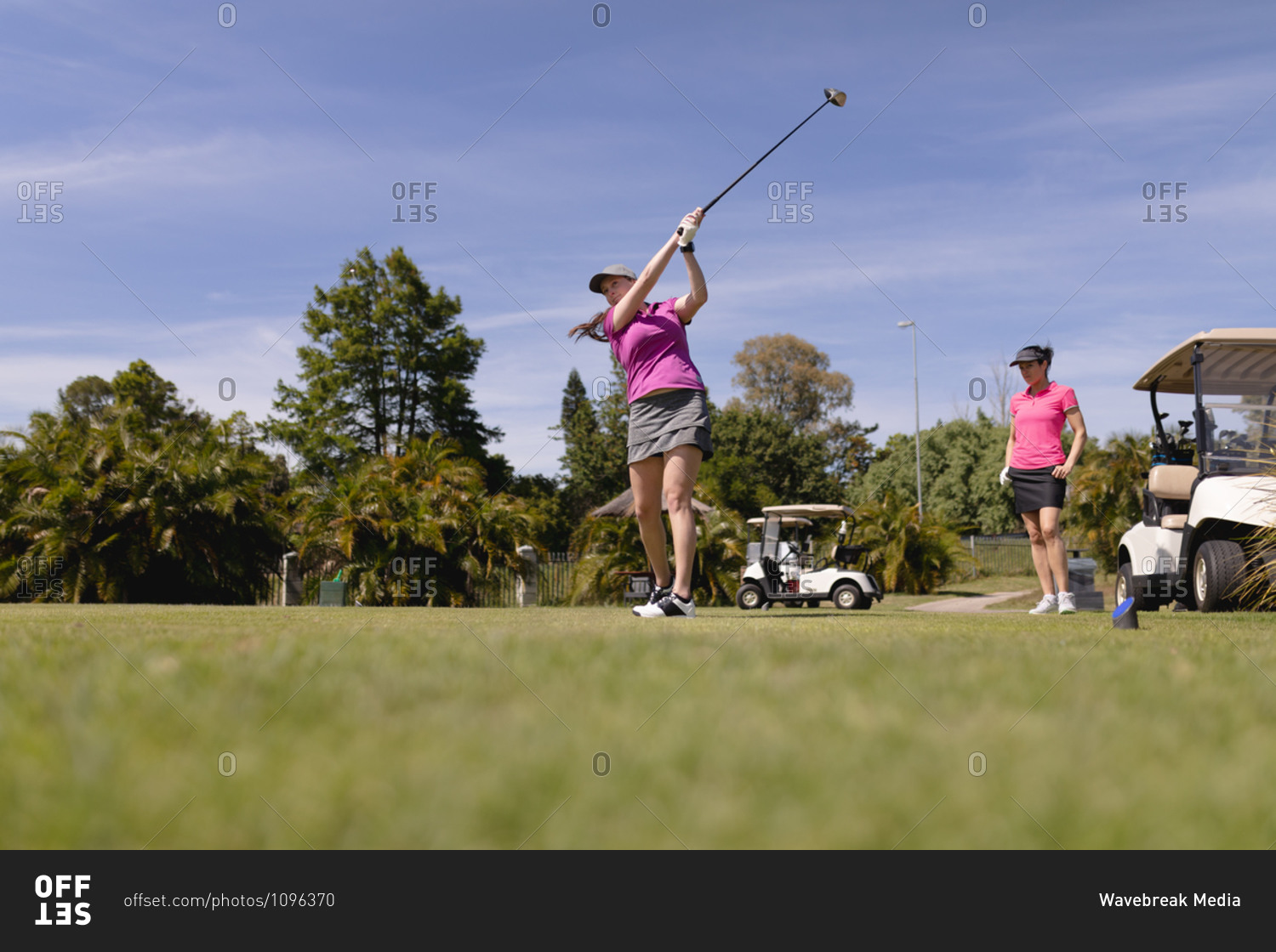 Two caucasian women playing golf one swinging club and taking a shot. sport leisure hobbies golf healthy outdoor lifestyle.