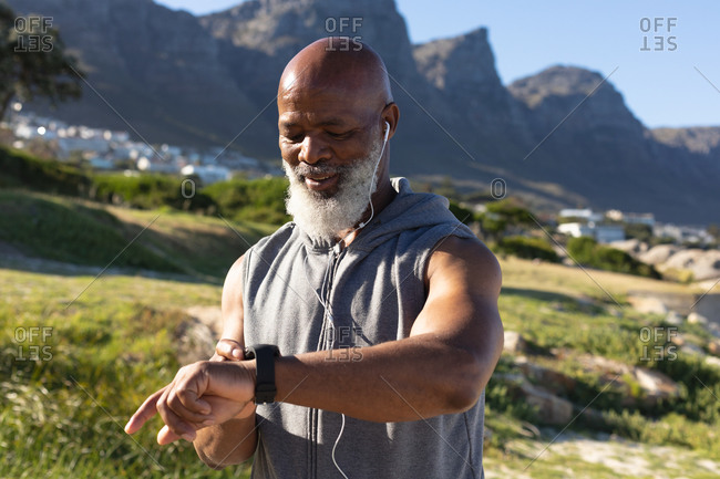 Fit senior African American man exercising wearing earphones checking smartwatch. healthy retirement technology communication outdoor fitness lifestyle.