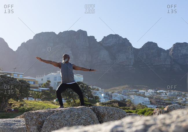 Fit senior African American man standing on rocky coast doing yoga. healthy retirement outdoor fitness lifestyle.