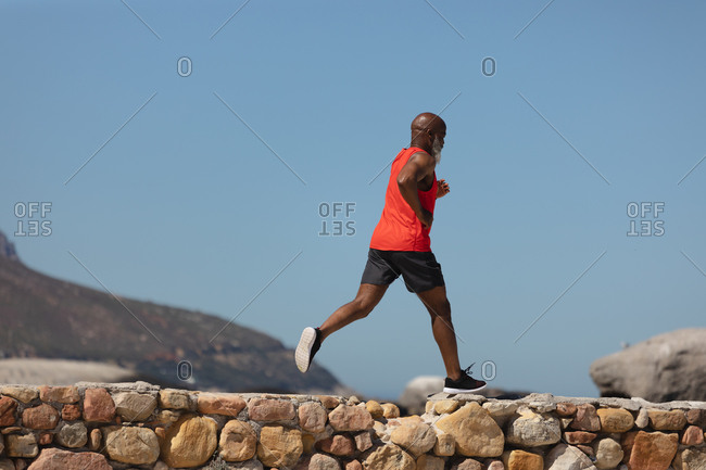 Fit senior African American man exercising running on coastal path. healthy retirement outdoor fitness lifestyle.