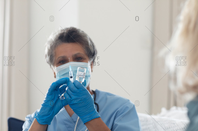 Senior African American female doctor wearing face mask preparing vaccination at home. healthcare hygiene protection during coronavirus covid 19 pandemic.