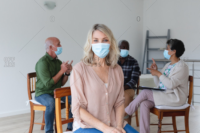 Diverse group of seniors wearing face masks talking during a group therapy session at home. health hygiene wellbeing at senior care home during coronavirus covid 19 pandemic.