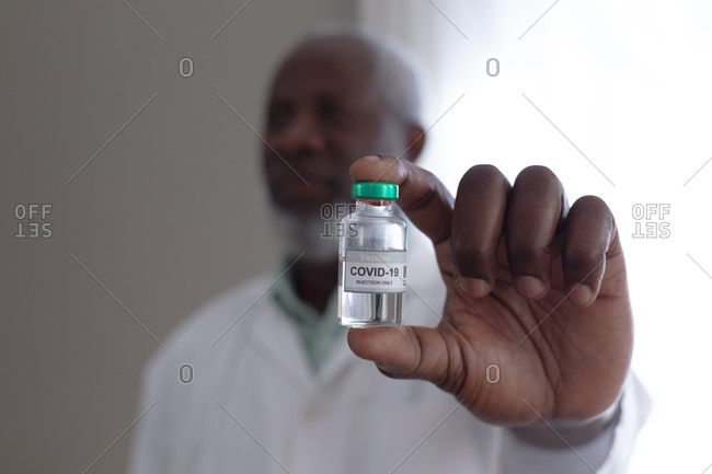 Senior African American male doctor holding covid 19 vaccine at patients home. healthcare at home in self isolation during quarantine lockdown.