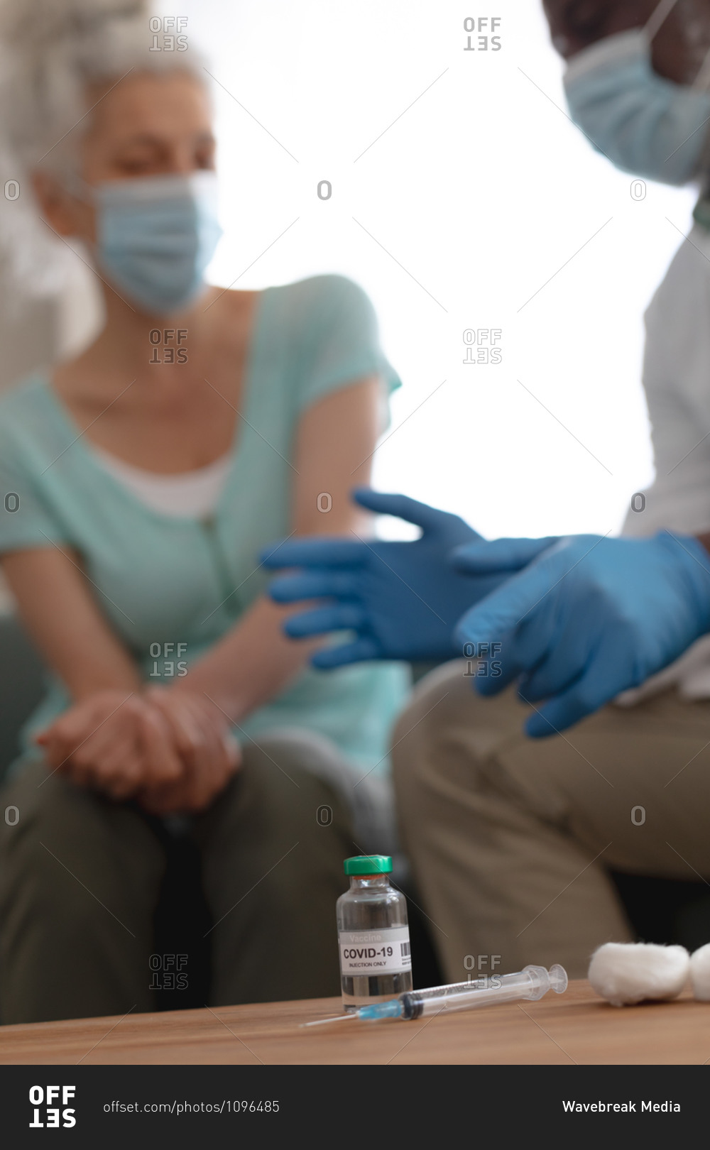 Senior African American male doctor preparing covid 19 vaccination for senior caucasian woman at home. healthcare and hygiene at home in self isolation during quarantine lockdown.