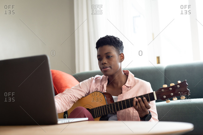 African American woman playing guitar while looking at the laptop at home. staying at home in self isolation in quarantine lockdown