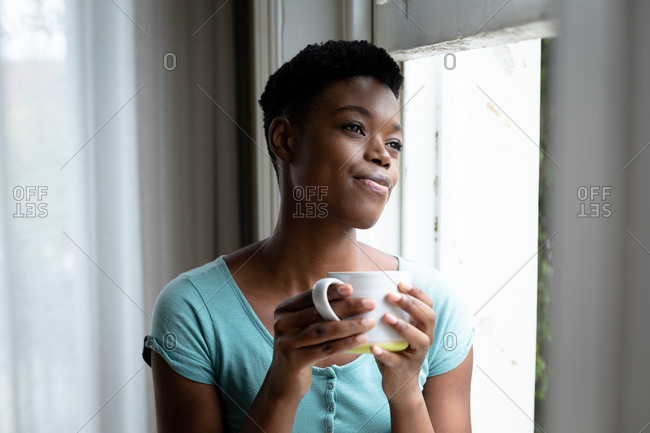 Portrait of African American woman holding coffee cup looking out of the window at home. staying at home in self isolation in quarantine lockdown