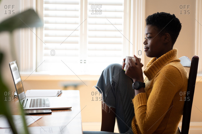 African American woman using laptop and drinking coffee in kitchen. staying at home in self isolation during quarantine lockdown.