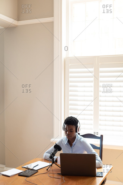 African American woman wearing headphones using microphone and laptop. communication online, staying at home in self isolation during quarantine lockdown.