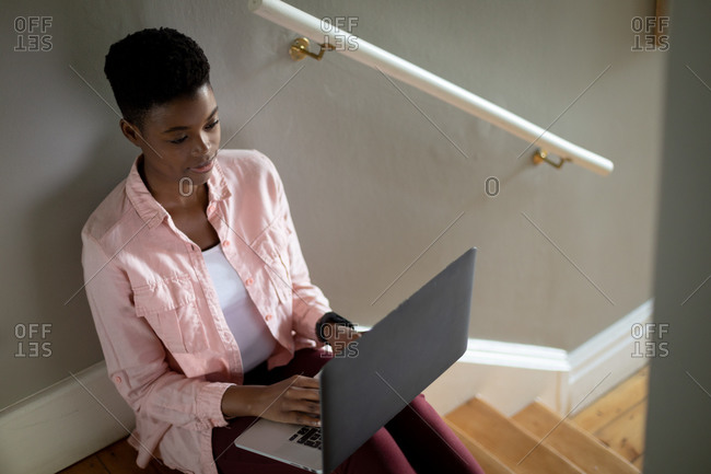 African American woman sitting on stairs using laptop working from home. staying at home in self isolation during quarantine lockdown.