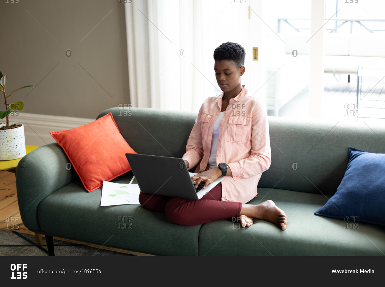 African American woman sitting on couch using laptop talking on ...