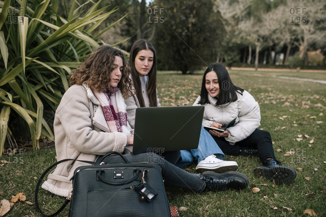 Three college girls studying sitting on the grass of the university campus