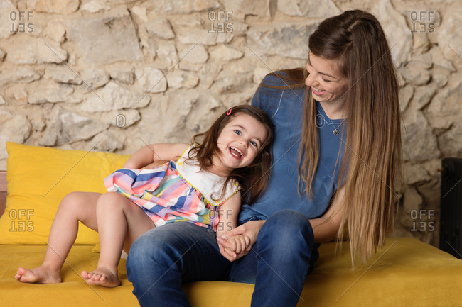 Smiling toddler playing with mother on yellow couch