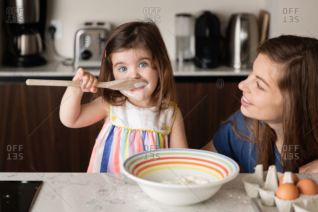 Mother looking at toddler girl tasting food in kitchen at home