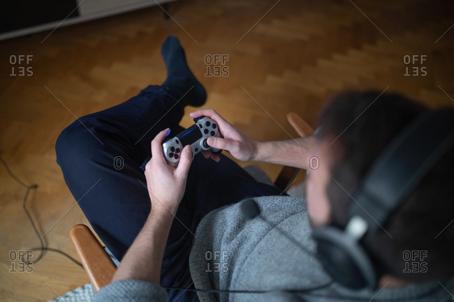 High angle view of a man sitting on chair in living room wearing a headset and playing video games