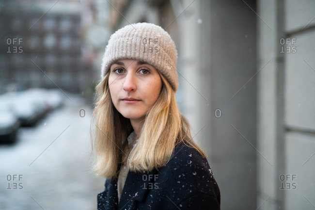 Blonde woman wearing knit hat and peacoat while walking on city street during snowfall