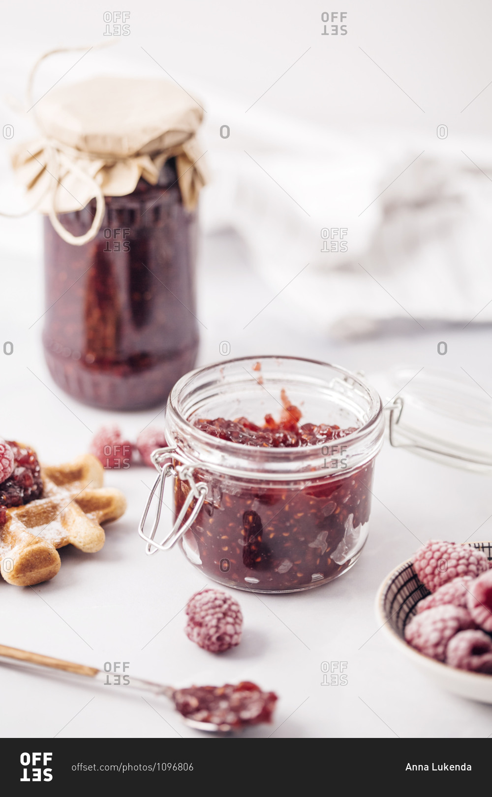 Frozen raspberries in bowl in front of a jar of homemade raspberry jam