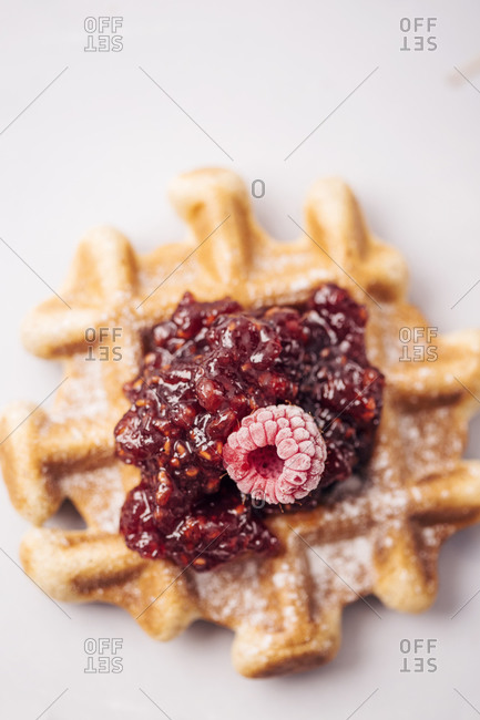 Frozen raspberries and homemade raspberry jam on the top of waffle