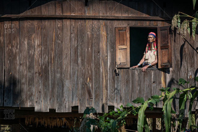 PADUANG PEOPLE, PAN PET VILLAGE, KAYAH STATE, MYANMAR - 24 November 2019: Portrait of old Kayan lady wearing brass coils placed around the neck, appearing to lengthen it, standing in window.
